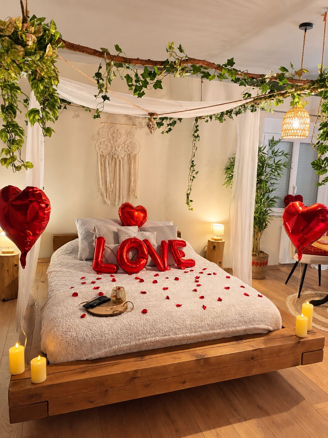 Ein Bett mit Baldachin, rote herzförmige Ballons, die 'LOVE' buchstabieren, und Kerzen.