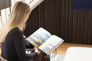 A person sitting on a chair reading a book in a room with a modern design, featuring a sloped ceiling and a wooden panel wall. - New Listing (Schlanders)