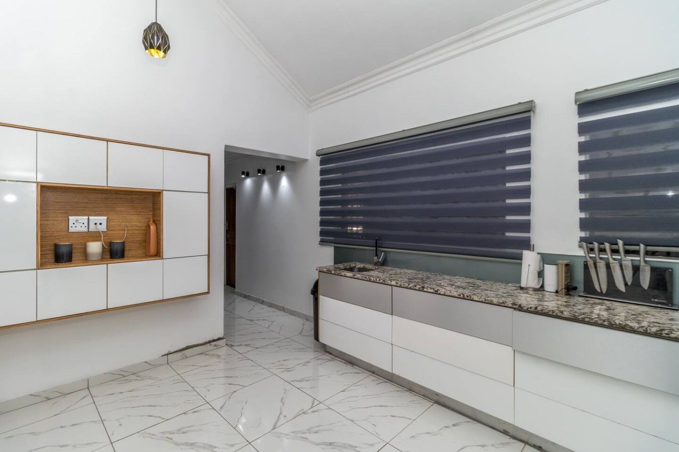 Una cocina moderna con armarios blancos, piso de mármol y un soporte empotrado para cuchillos.
