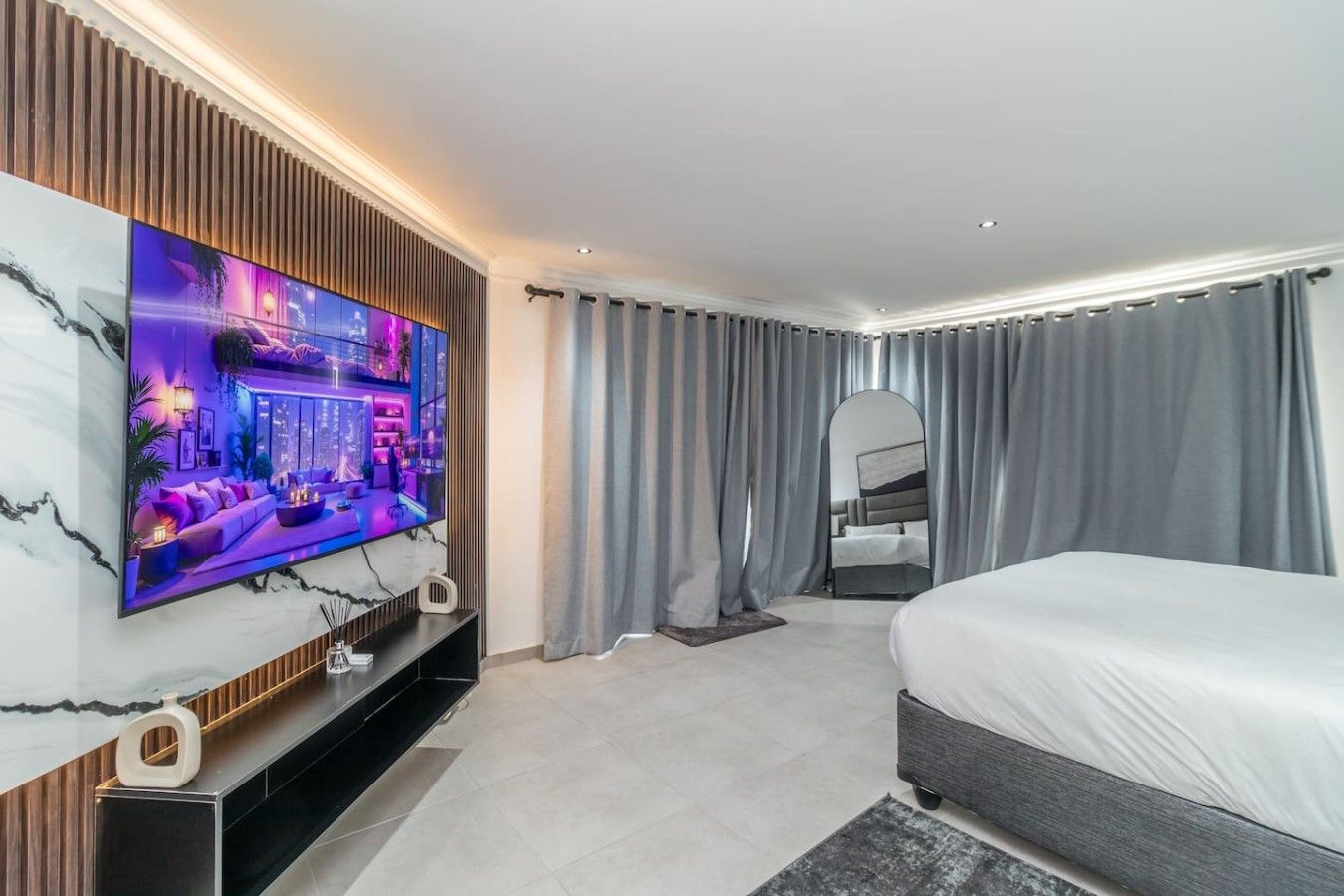 Une chambre d’hôtel moderne dotée d’une grande télévision à écran plat, d’un lit, d’un coin salon et d’une salle de bain.