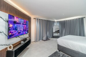 Une chambre d’hôtel moderne dotée d’une grande télévision à écran plat, d’un lit, d’un coin salon et d’une salle de bain.