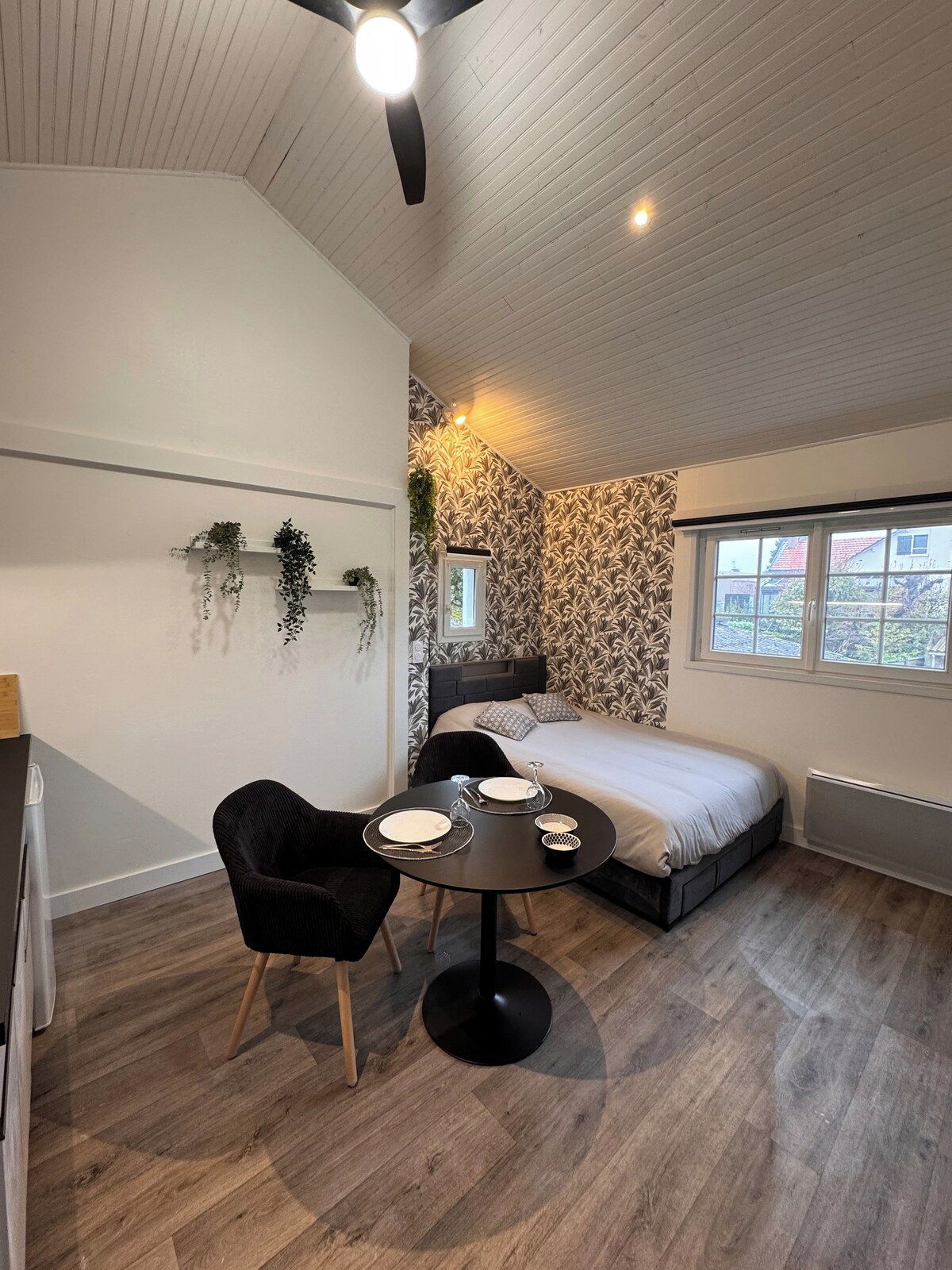 Une chambre à coucher avec un lit, une table à manger avec des chaises, un ventilateur de plafond et une fenêtre donnant sur un beau paysage.