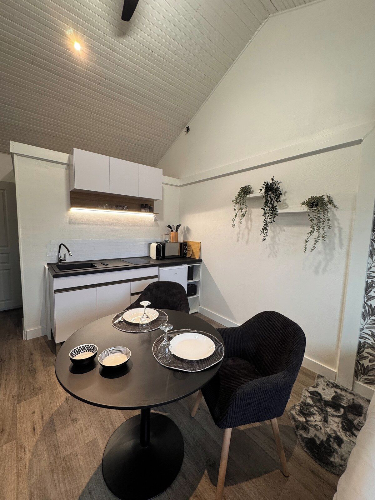 Une cuisine moderne avec des meubles blancs, un plan de travail noir et un coin repas comprenant une table ronde et deux chaises.