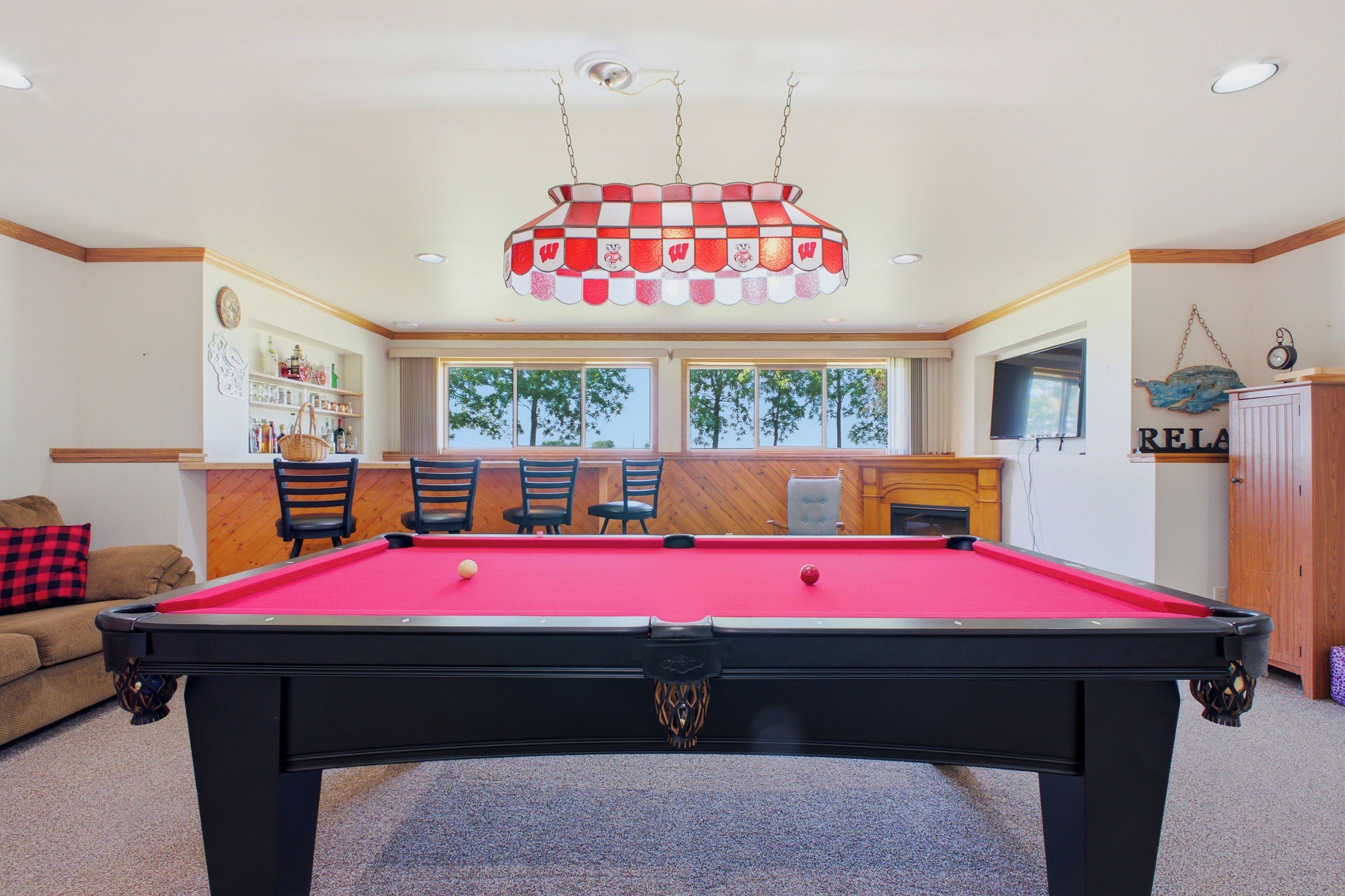 A pool table with chairs, a bar area, and a view of trees through large windows.