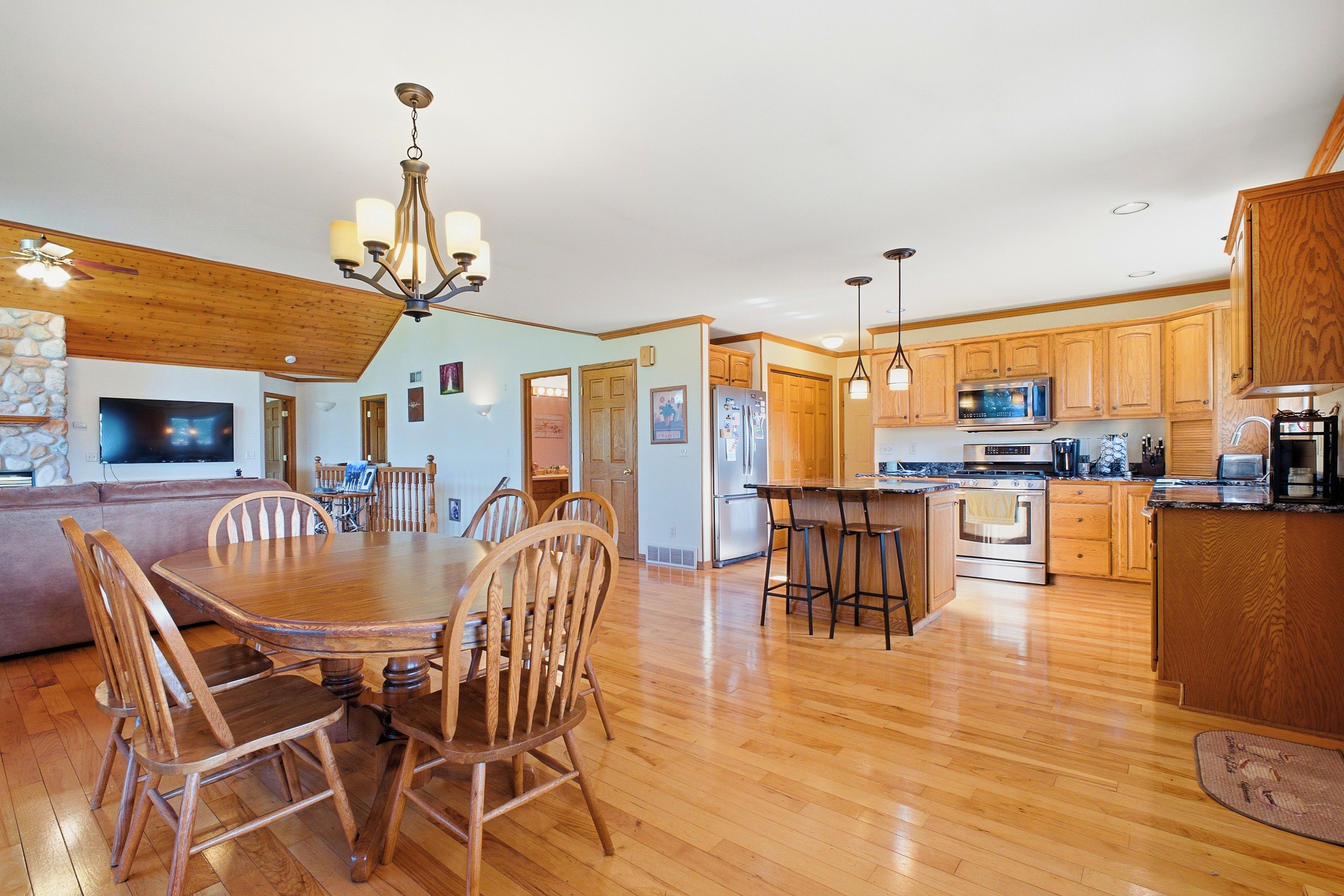 A spacious kitchen with wooden cabinets, a dining area with a wooden table and chairs, and a living room with a flat-screen TV.