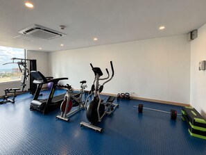 Ett gym med träningsutrustning, ett blått gummigolv och ett fönster med utsikt.