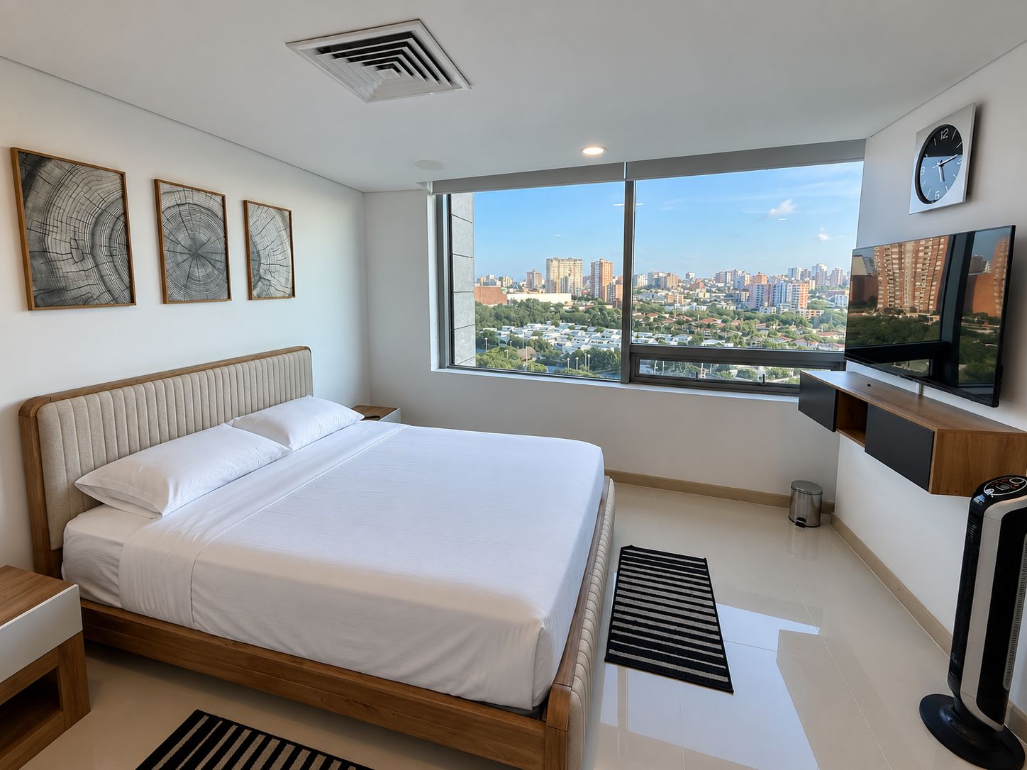 A modern bedroom with a city view, a bed, a TV, and artwork on the wall.