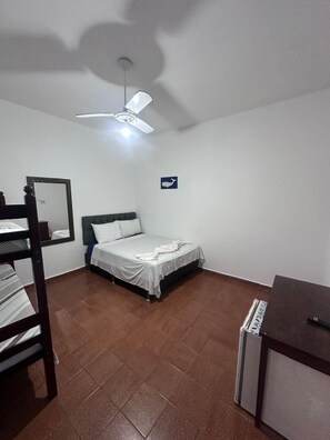 Una camera da letto con un letto, una scrivania, una sedia, una ventola a soffitto e uno specchio fissato alla parete.