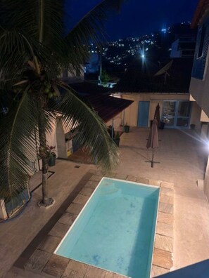 Una piscina con bordo piastrellato, circondata da palme e un edificio con una porta blu.