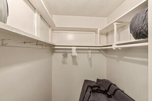 Ein Kleiderschrank mit Ablagefläche und Regalen, gefüllt mit Kleidung und Taschen.