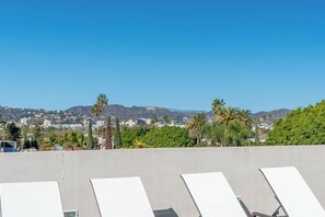 A rooftop with lounge chairs, a clear sky, and a cityscape with mountains in the background. - Casa Jenn by Oraklus (Beverly Hills)