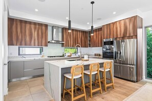 A modern kitchen with a central island, bar stools, stainless steel appliances, and wooden cabinetry. - Casa Jenn by Oraklus (Beverly Hills)