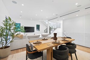 A modern dining area with a wooden table set for four, a potted plant, and a white sofa in the background. - Casa Jenn by Oraklus (Beverly Hills)