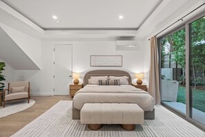 A modern bedroom with a large bed, bedside lamps, a bench, and a view of the outdoors. - Casa Jenn by Oraklus (Beverly Hills)