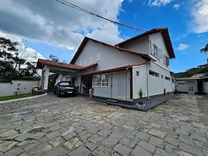 A two-story house with a tiled roof, a car parked in the driveway, and a stone-paved courtyard.