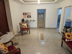 A spacious living area with a dining table, a sofa, a water dispenser, and a staircase leading to an upper floor.