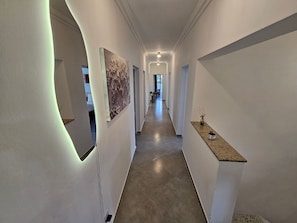 A hallway with a light fixture, a painting, and a plant on a shelf.