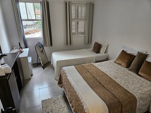 Una habitació d'hotel amb dos llits, un escriptori amb una cadira, una taula petita amb una ampolla i gots, i una finestra amb persianes.