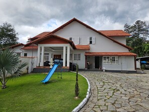 Una casa de dues plantes amb teulada vermella, un porxo frontal i un tobogan blau al jardí davanter.