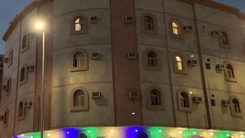 Un edificio de varios pisos con ventanas arqueadas y unidades de aire acondicionado, iluminado por luces de calle y luces decorativas.