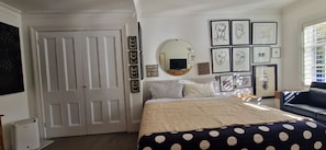 Ein Schlafzimmer mit einem Bett, einem Schminktisch, einem Spiegel und gerahmten Kunstwerken an der Wand.