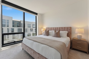Een moderne hotelkamer met een groot bed, twee bedlampen en uitzicht op een gebouw door een groot raam.