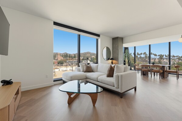 A spacious living room with a large window, a round glass coffee table, and a modern sofa.