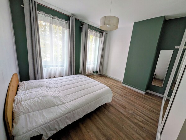 A bedroom with a bed, a window with curtains, a hanging light fixture, and a mirror on the wall.