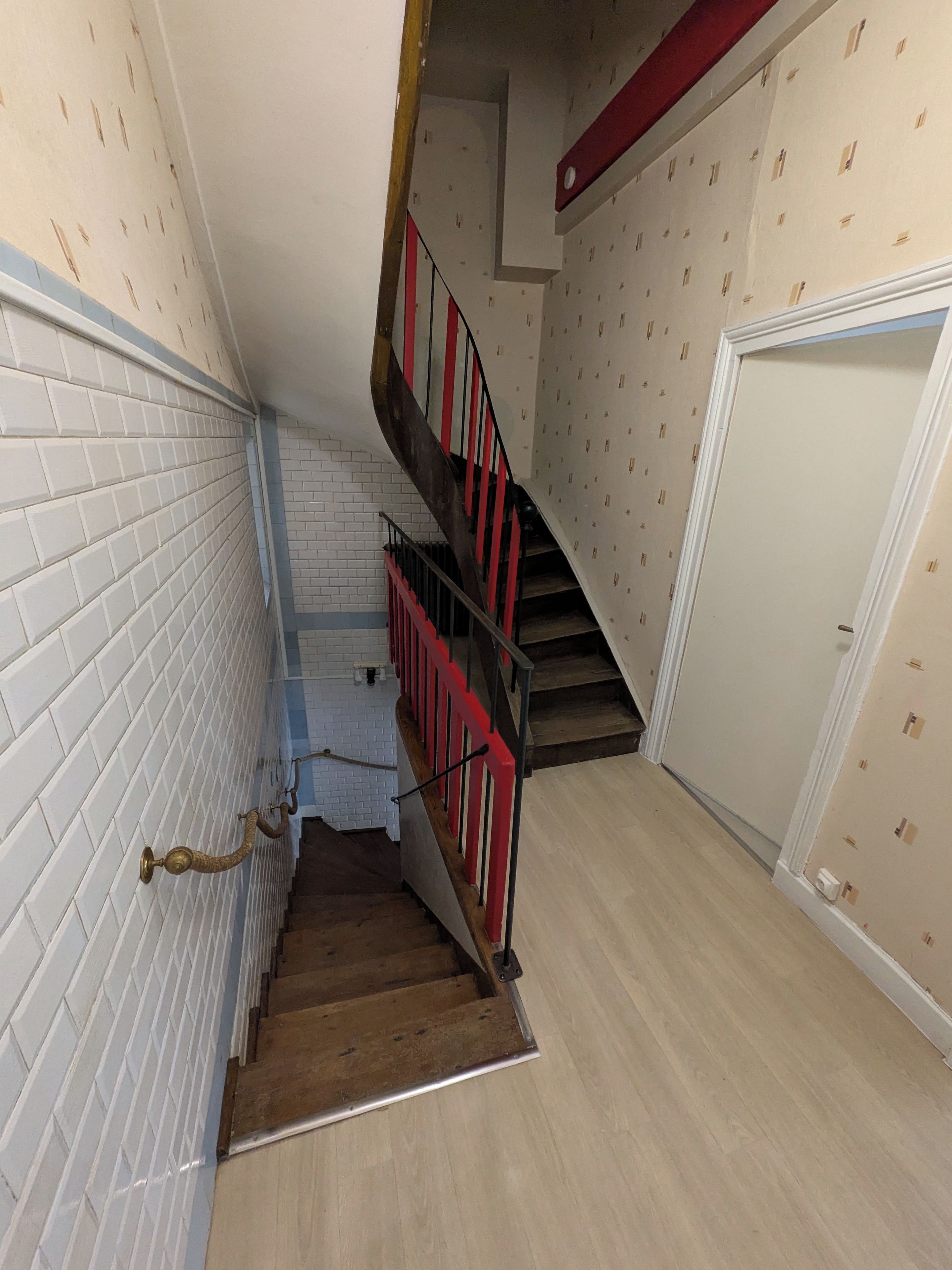 Punaisella kaiteella varustetut portaat johtavat ylätasanteelle, jossa on valkoinen ovi ja seinä, jossa on kuvioitu pinta.