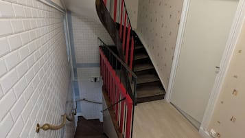 Punaisella kaiteella varustetut portaat johtavat ylätasanteelle, jossa on valkoinen ovi ja seinä, jossa on kuvioitu pinta.