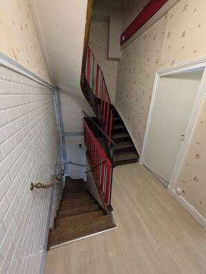 A staircase with a red railing leading to a landing, a white door, and a wall with a patterned design. - New Listing (Charolles)