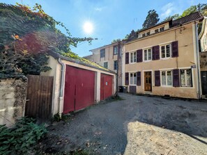 A narrow street with a red garage door, a two-story building with shutters, and a clear sky. - New Listing (Charolles)