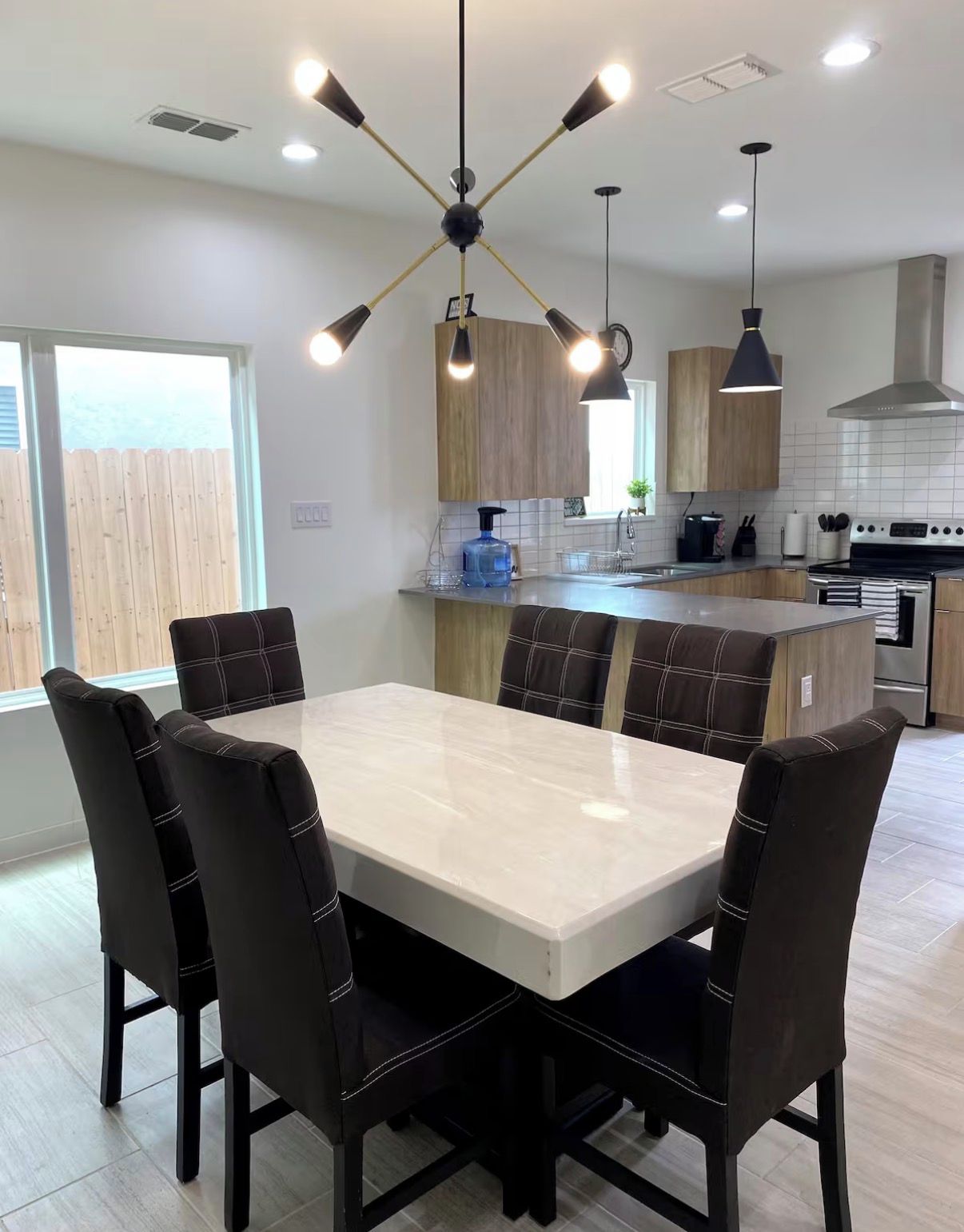 Una cocina moderna con una isla central, iluminación colgante y un área de comedor con una mesa de mármol y sillas tapizadas.