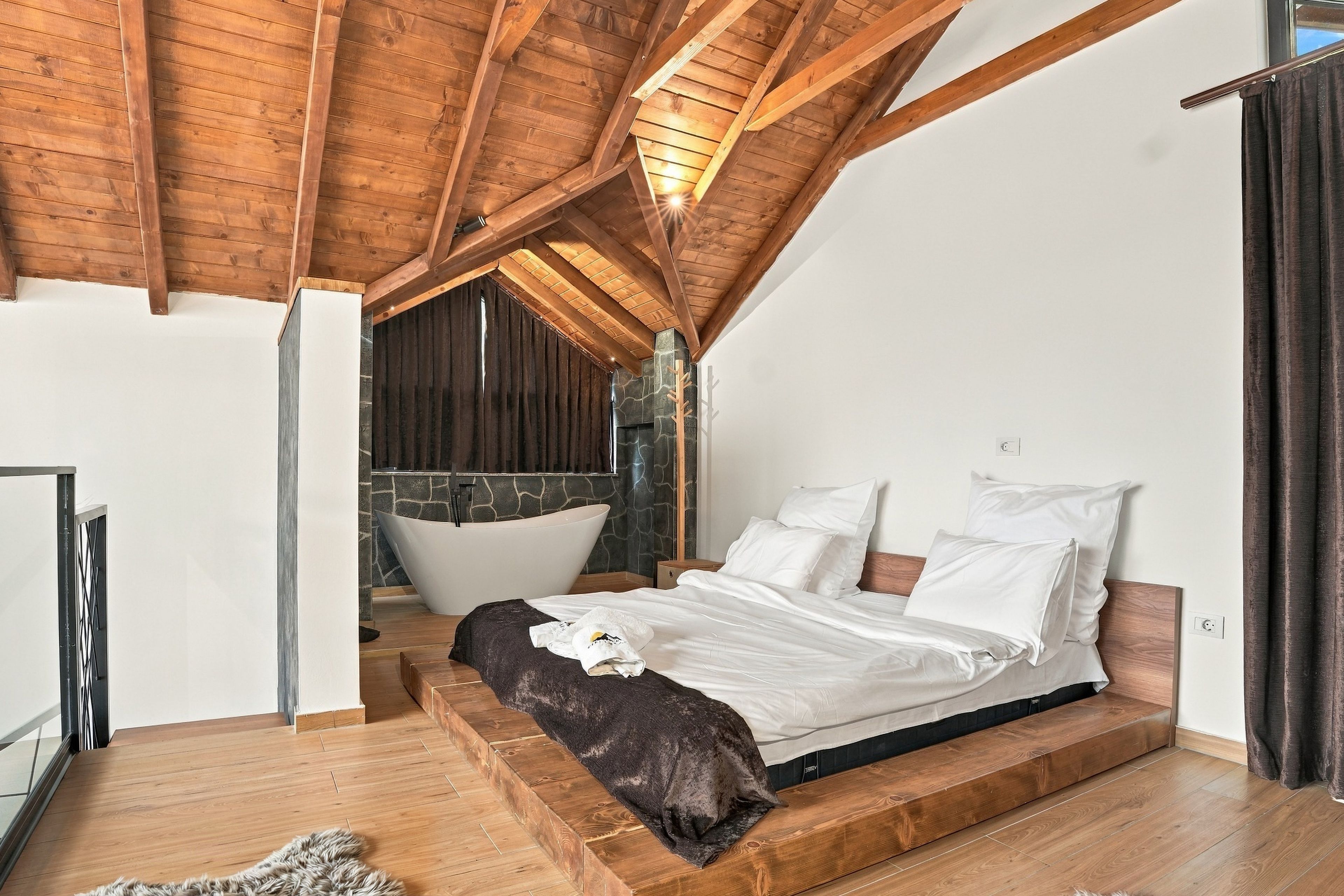 Een slaapkamer met een schuine kap, een groot bed, een stenen muur en een bad.