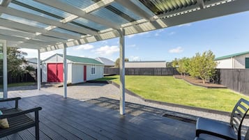 Un espacio al aire libre cubierto con piso de madera, un cobertizo rojo y un patio con césped.