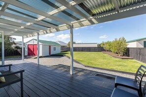 Un espacio al aire libre cubierto con piso de madera, un cobertizo rojo y un patio con césped.