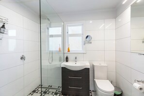 Un baño moderno con cabina de ducha de vidrio, un lavabo blanco con espejo y un inodoro.