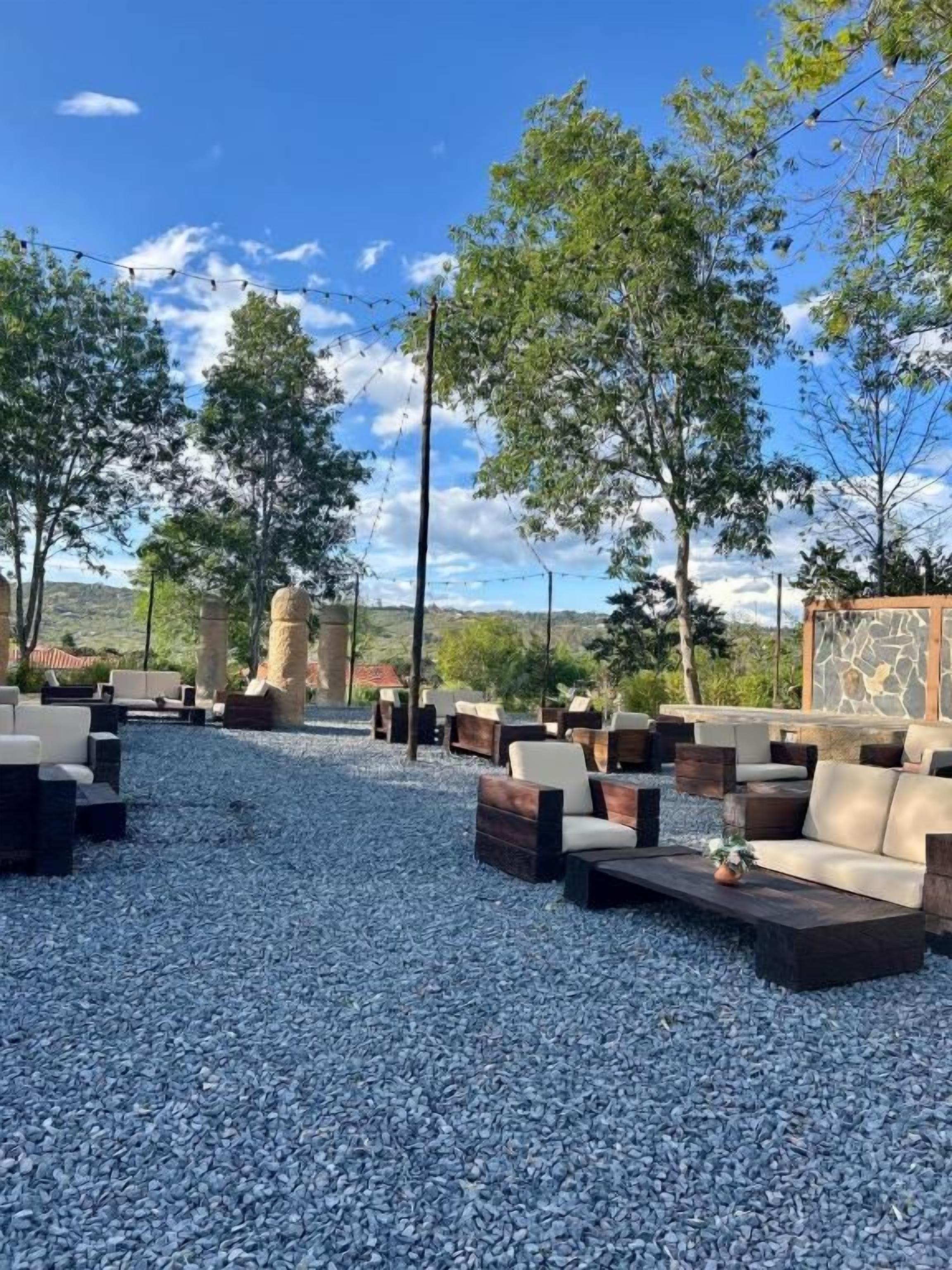 Un espace extérieur aménagé avec des canapés et des tables, entouré d’arbres et offrant une vue sur un ciel dégagé.