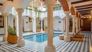 Zona de piscina con suelo a cuadros, columnas y plantas en macetas.