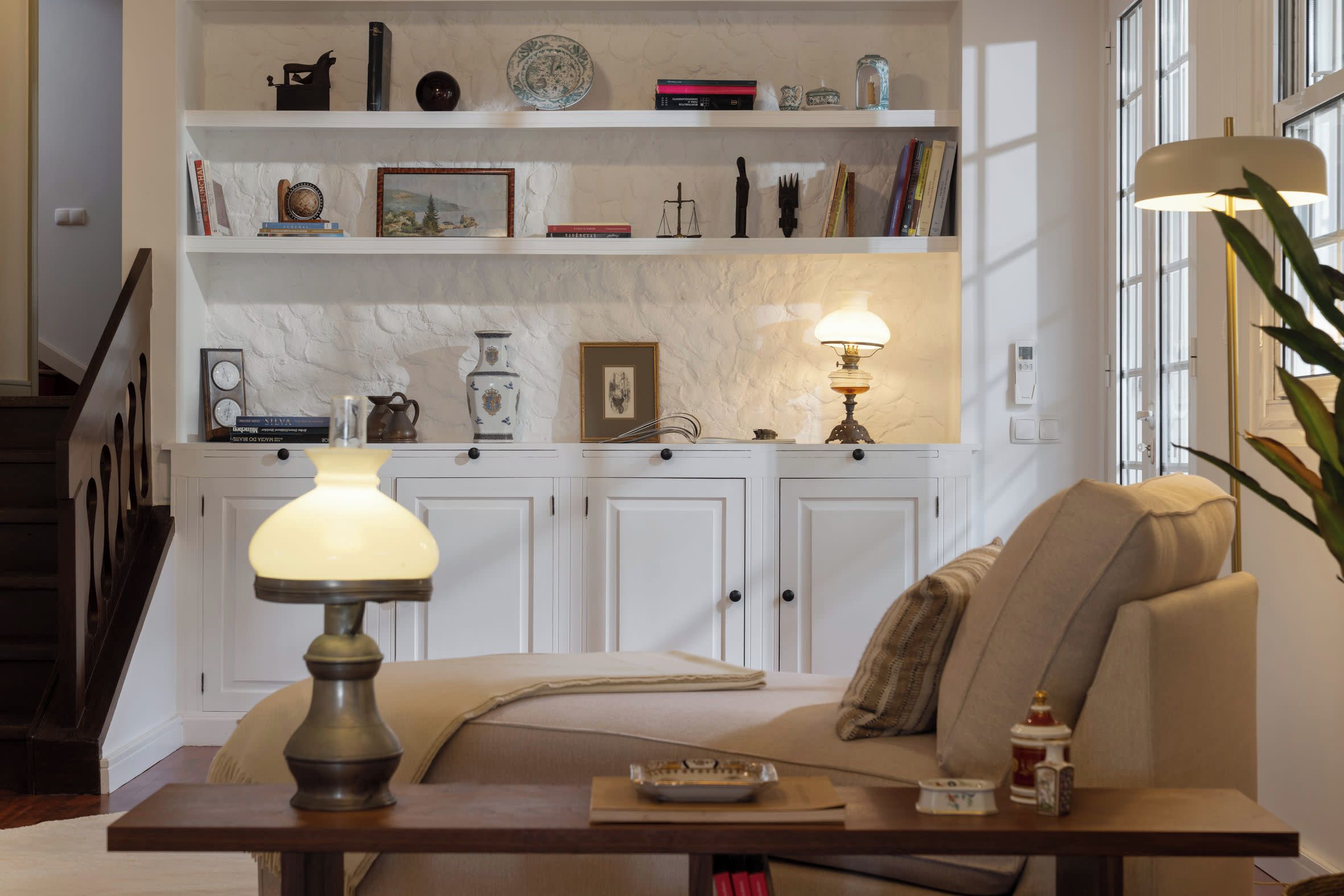 A living room with a sofa, a coffee table, and a lamp. There are shelves above the sofa with various items.