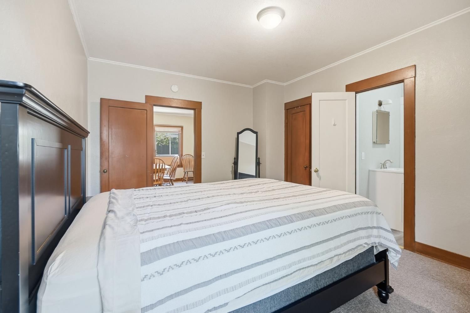 A bedroom with a bed, a wardrobe, a mirror, a door, and a window.