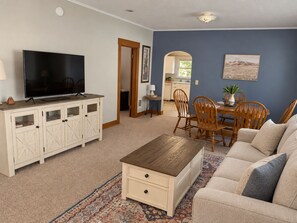 Een woonkamer met een televisie, een houten kast, een bank en een eethoek met stoelen en een tafel.