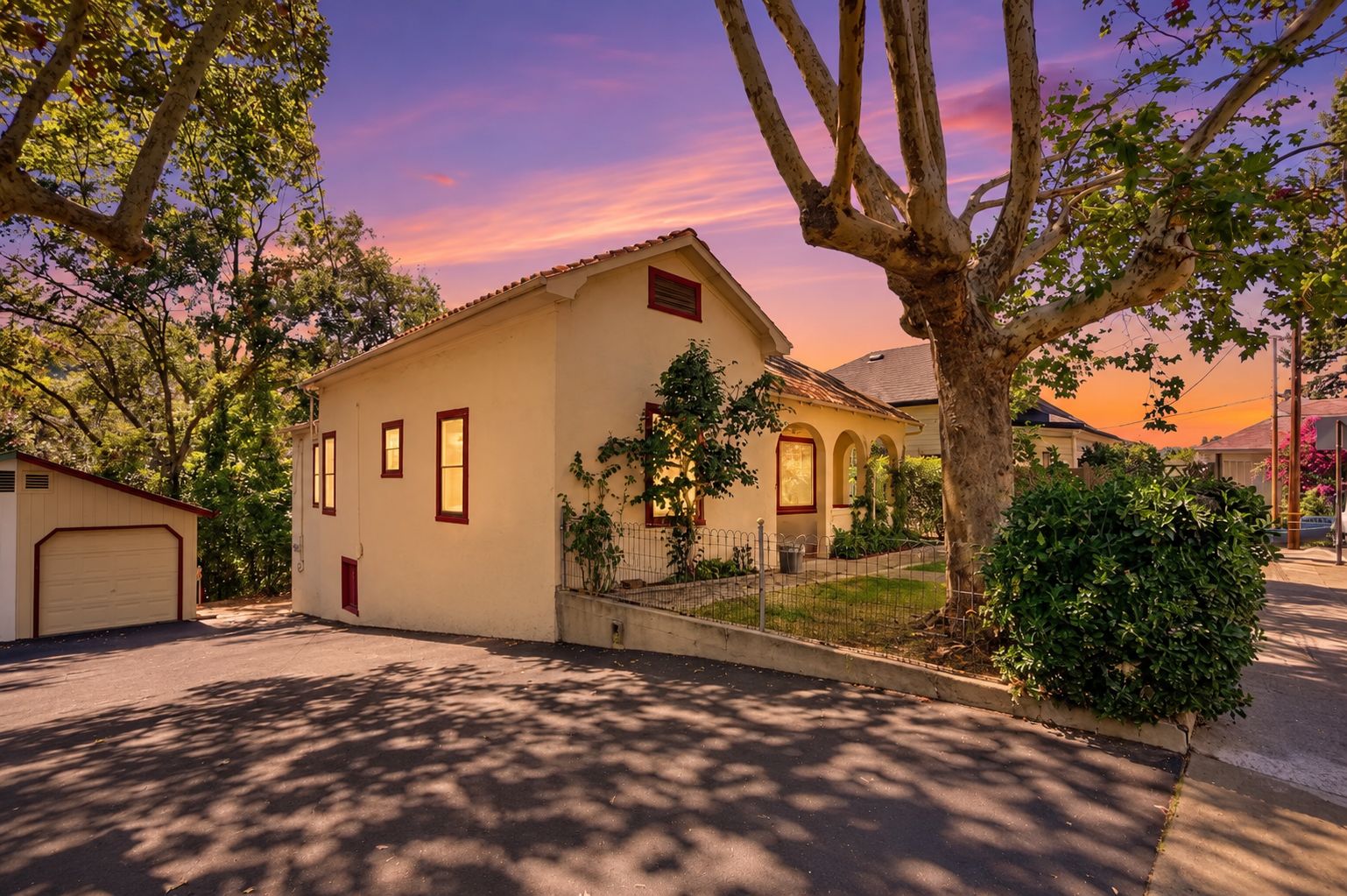 Une maison d’habitation avec un garage, une cour clôturée et un arbre au premier plan.