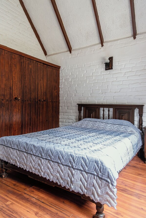 A bedroom with a wooden bed, a white brick wall, and a wooden wardrobe.