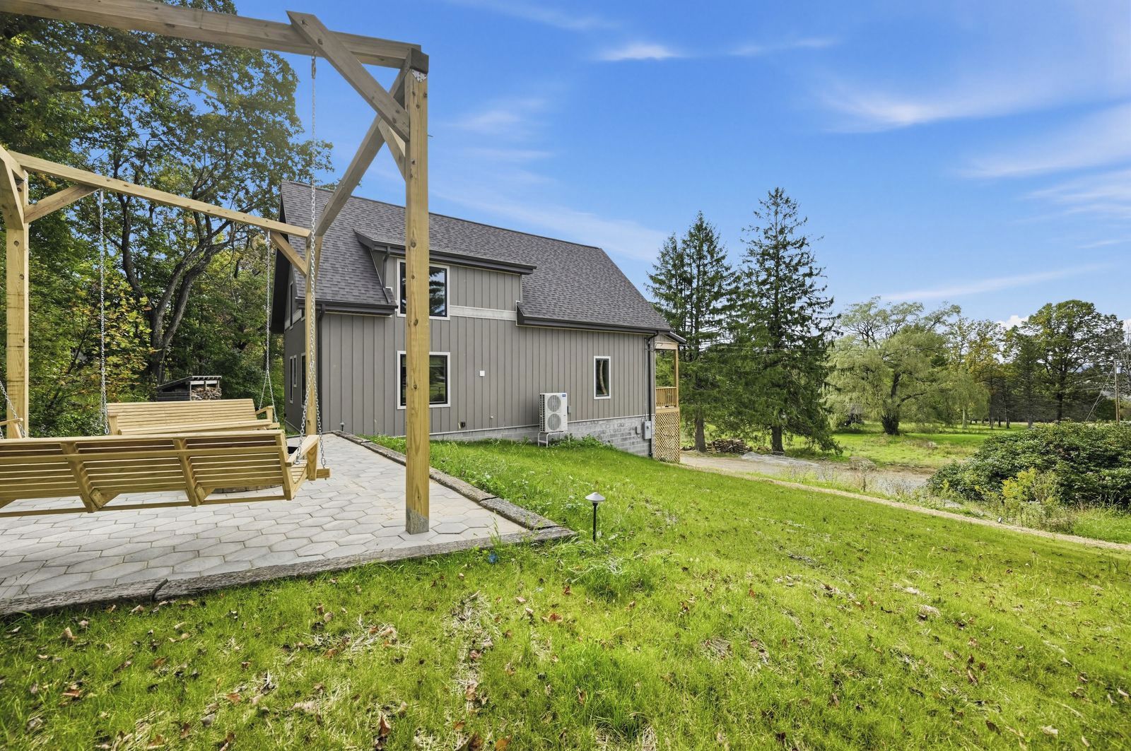 A residential property with a wooden swing set, a paved patio, and a house with a grey exterior.