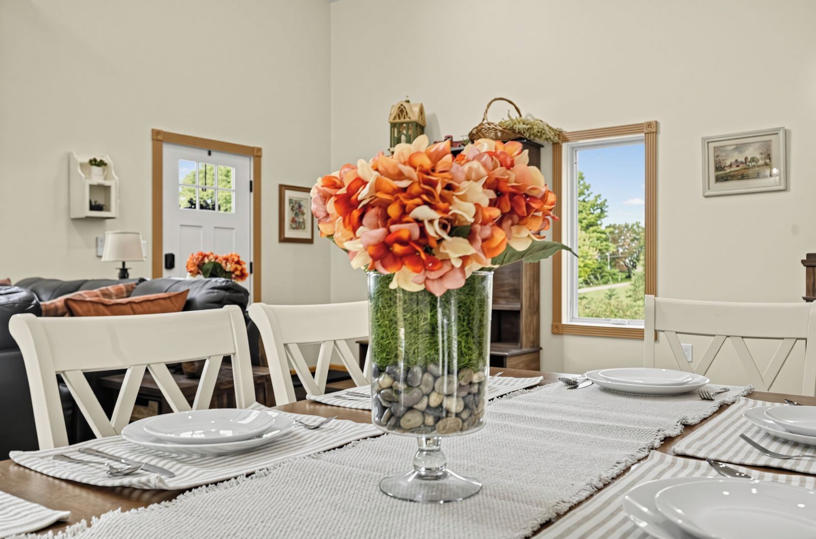 Un coin repas avec une table dressée pour quatre personnes, un vase de fleurs et une vue sur l’extérieur par une fenêtre.