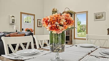 Un coin repas avec une table dressée pour quatre personnes, un vase de fleurs et une vue sur l’extérieur par une fenêtre.