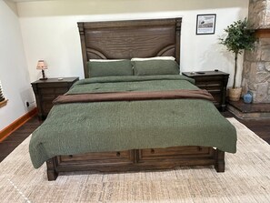Quarto com uma cama grande, cabeceira de madeira, duas mesas de cabeceira, um criado-mudo, uma luminária, um quadro emoldurado e uma planta em vaso.
