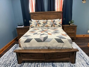 Una cama con colcha de estampado geométrico, cabecera de madera y mesitas de noche con lámparas.