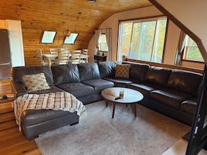 Ein gemütliches Wohnzimmer mit einem ledernen Ecksofa, einem kleinen runden Couchtisch und einer Holzbalkendecke.